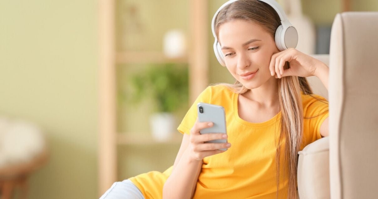 Mujero jóven rubia escuchando música con auriculares mientras practica preposiciones en inglés.
