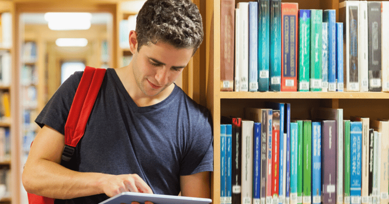 Hombre joven  empezando a aprender inglés desde su tablet en una biblioteca