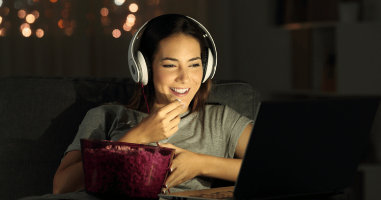 Mujer joven con pochoclos aprendiendo inglés viendo películas desde su laptop