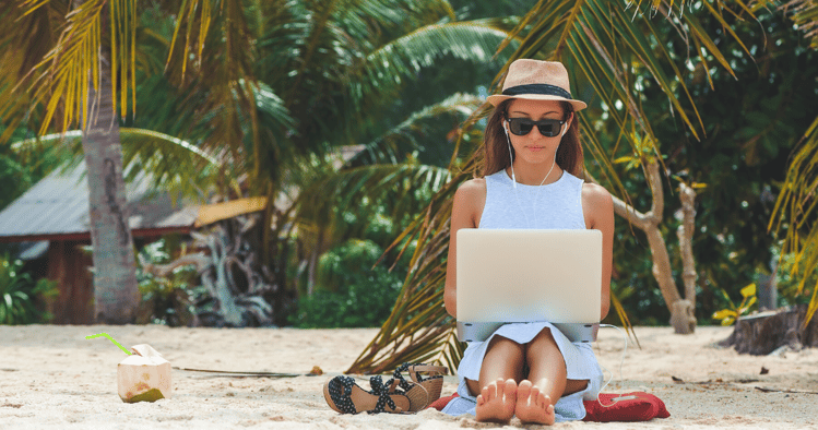 Mujer joven en la playa con su laptop estudiando vocabulario en inglés para el verano