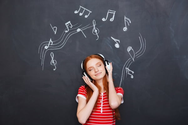 Relaxed smiling beautiful young woman listening to music in headphones over chalkboard background