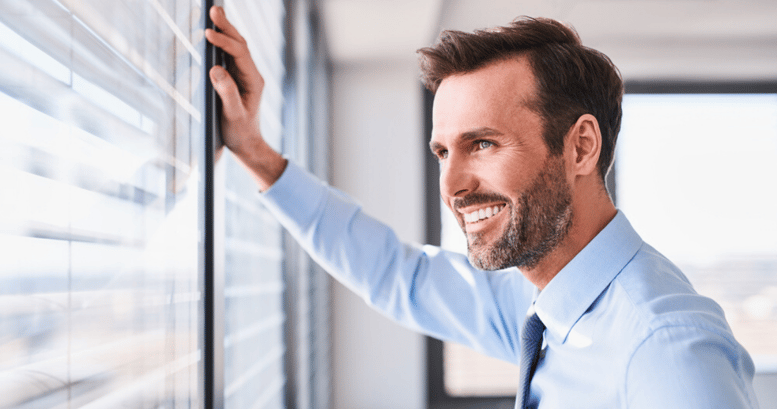 Trabajador vestido de traje mirando por la ventana feliz porque puede hablar en inglés con clientes y colaboradores