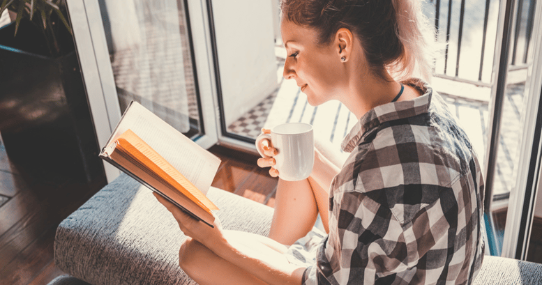 Una joven mujer leyendo un libro con una taza de cafe para adquirir mejor vocabulario en inglés