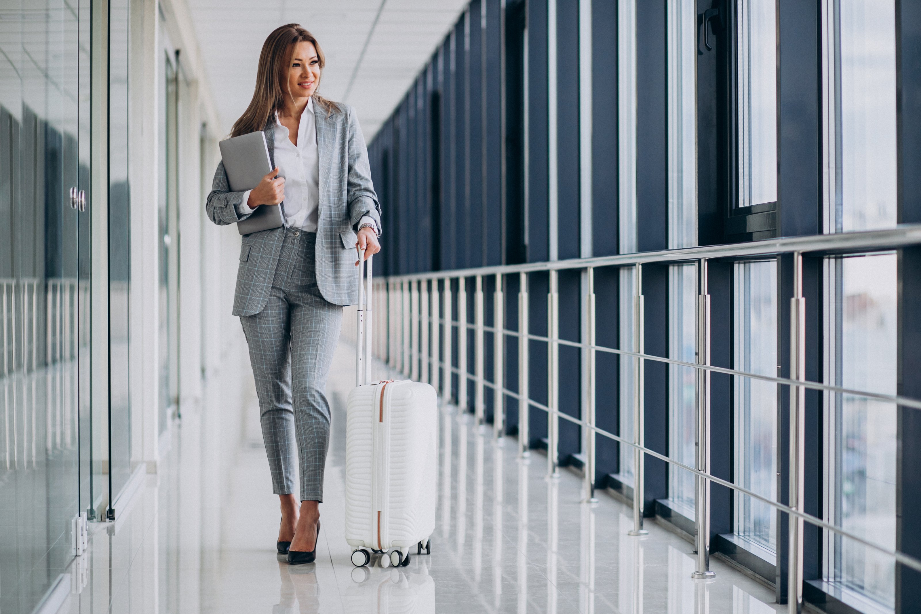 business-woman-with-travel-luggage-in-airport-holding-laptop